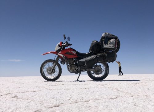 Motorrad und Fahrerin auf Salzwüste in Bolivien während Motorradreise durch Südamerika, Motorrad wirkt durch Perspektive größer