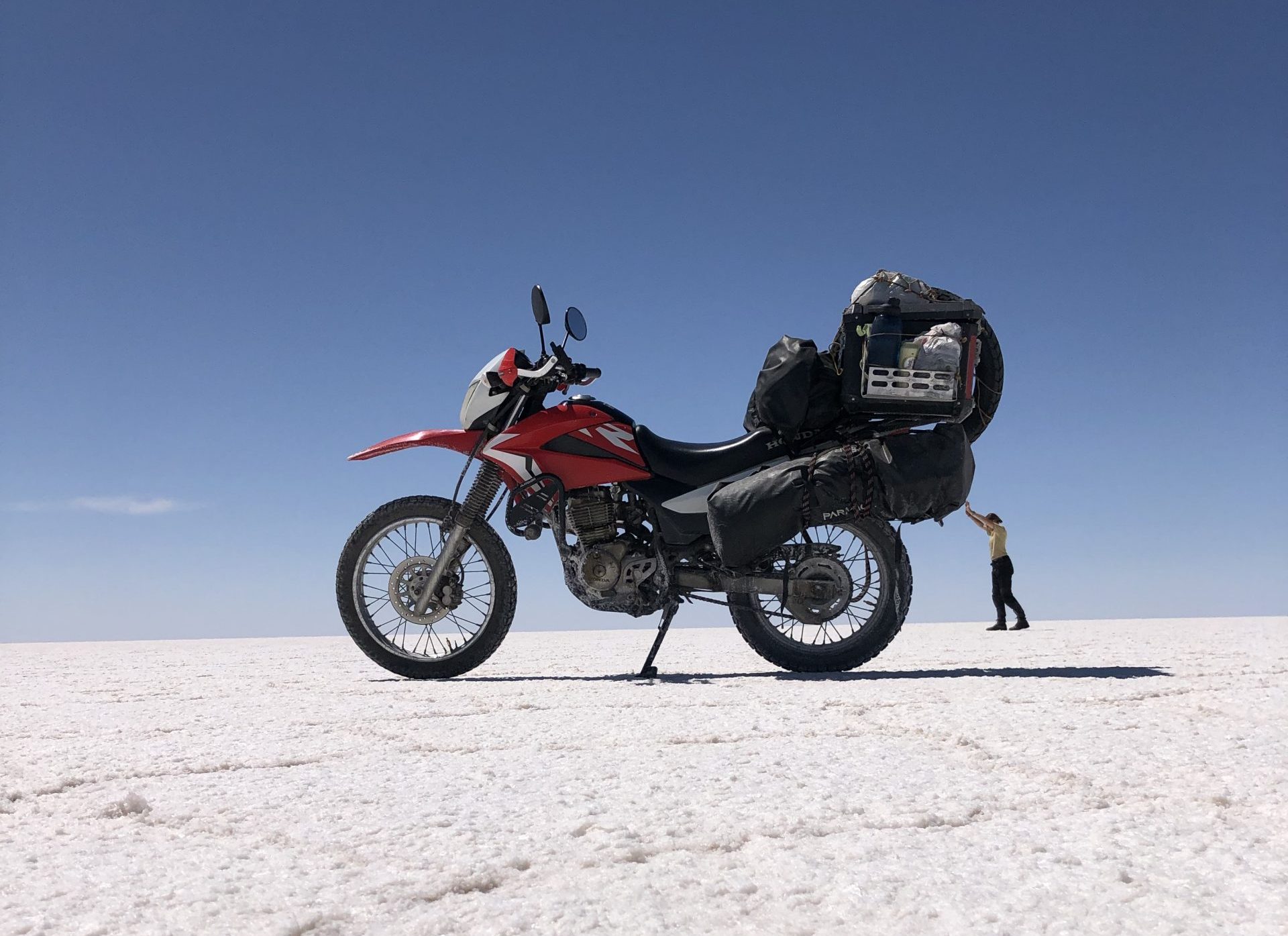 Motorrad und Fahrerin auf Salzwüste in Bolivien während Motorradreise durch Südamerika, Motorrad wirkt durch Perspektive größer