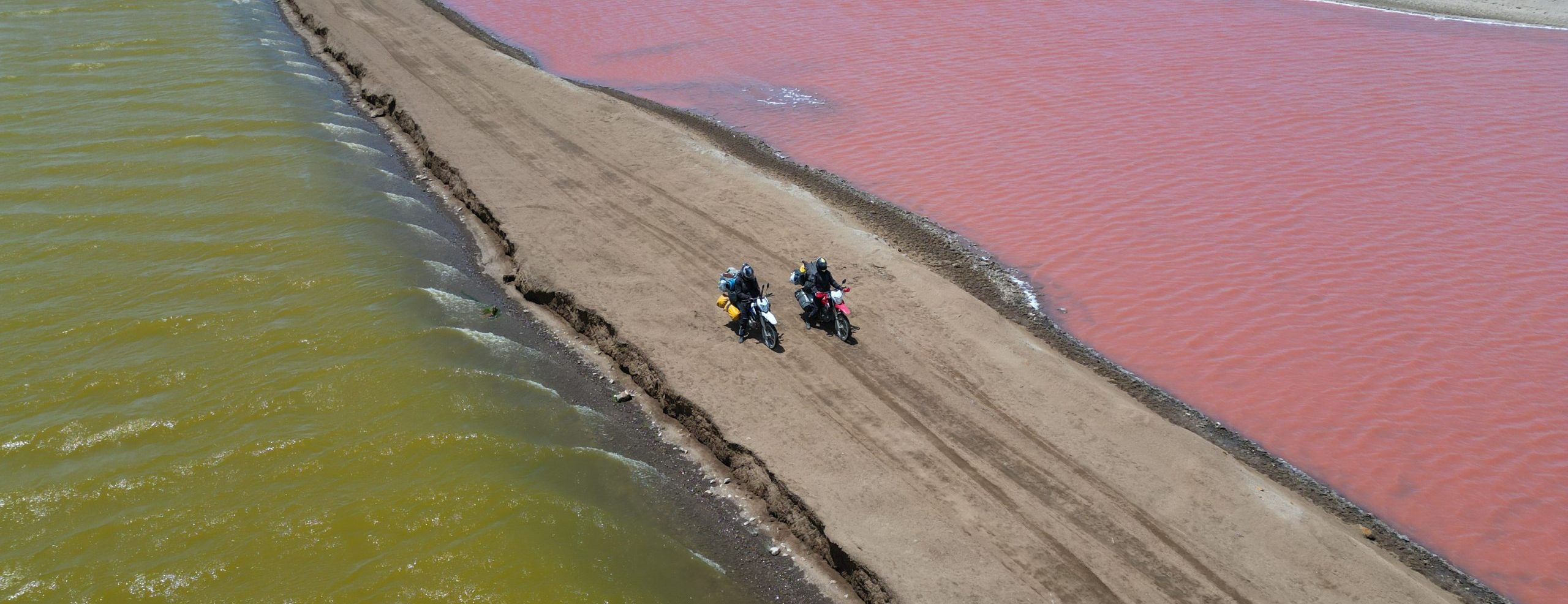 Zwei Motorradfahrer auf Feldweg in Peru zwischen pinker und grüner Lagune während Motorradreise durch Südamerika