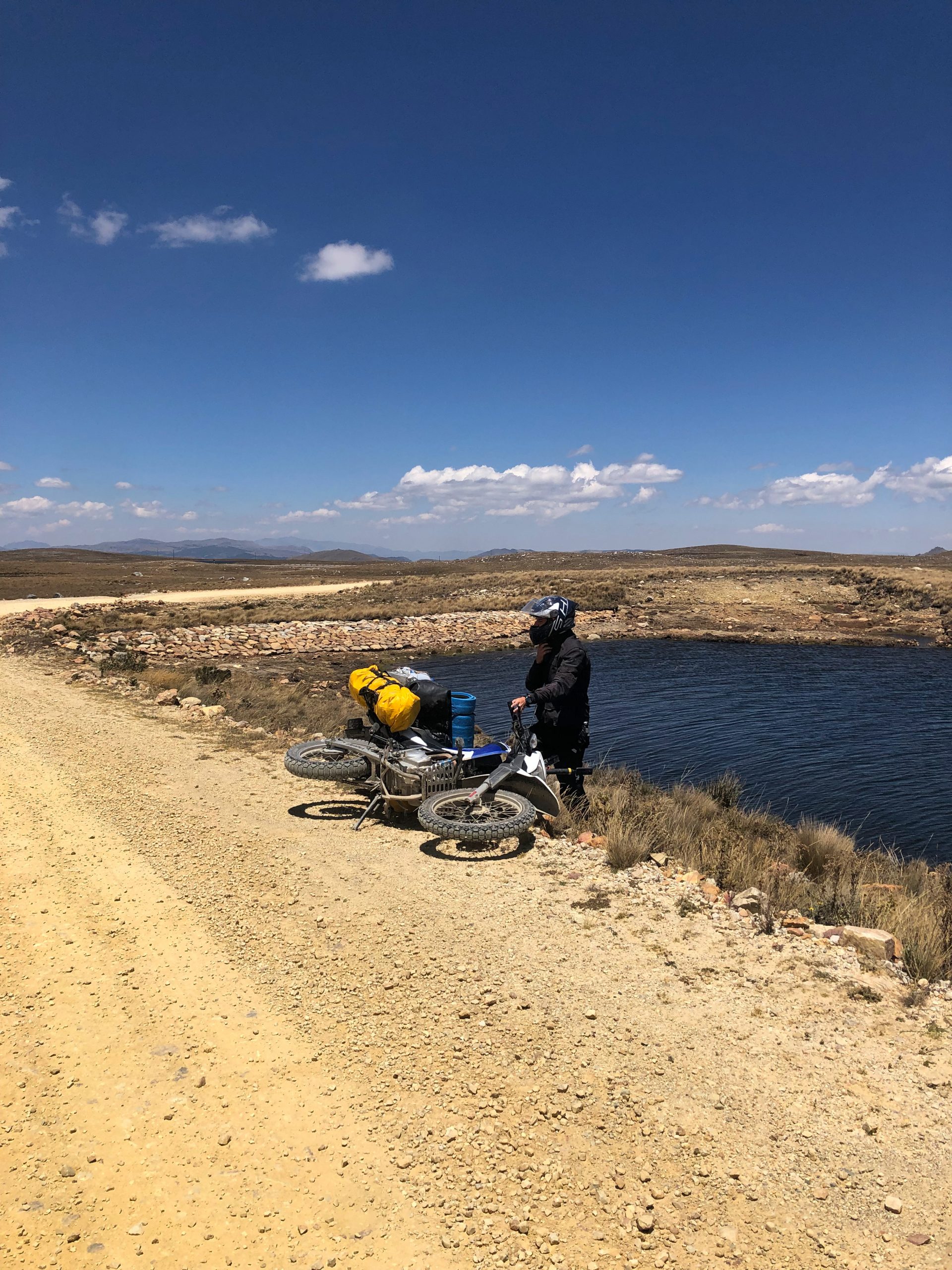 Umgefallenes Motorrad auf Schotterstraße auf Hochplateau in Peru mit Fahrer im Hintergrund während Motorradreise durch Südamerika