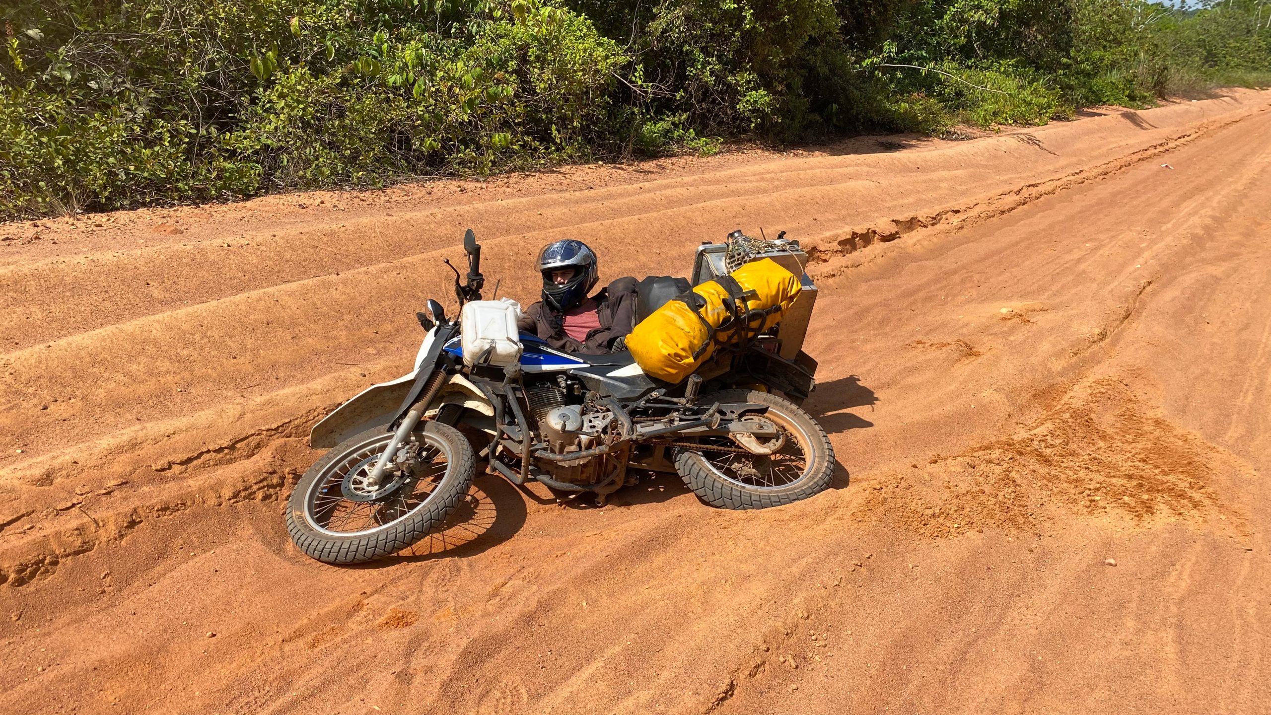 Motorradfahrer liegt mit Motorrad im Sand auf sandiger Straße in Brasilien während Motorradreise durch Südamerika